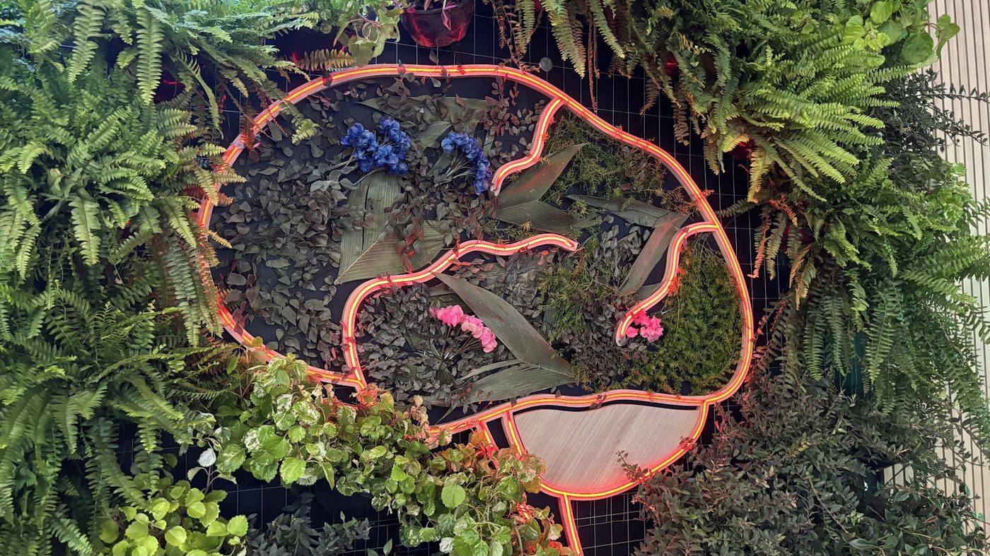 Detalhe de cenografia com neon verde e folhagens decorativas em evento corporativo