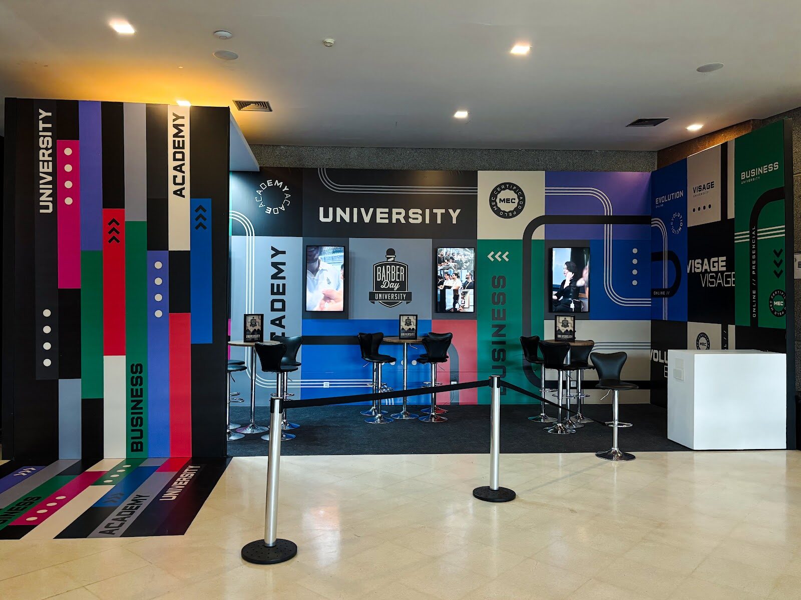 Espaço lounge com paredes geométricas coloridas e banquetas em evento corporativo