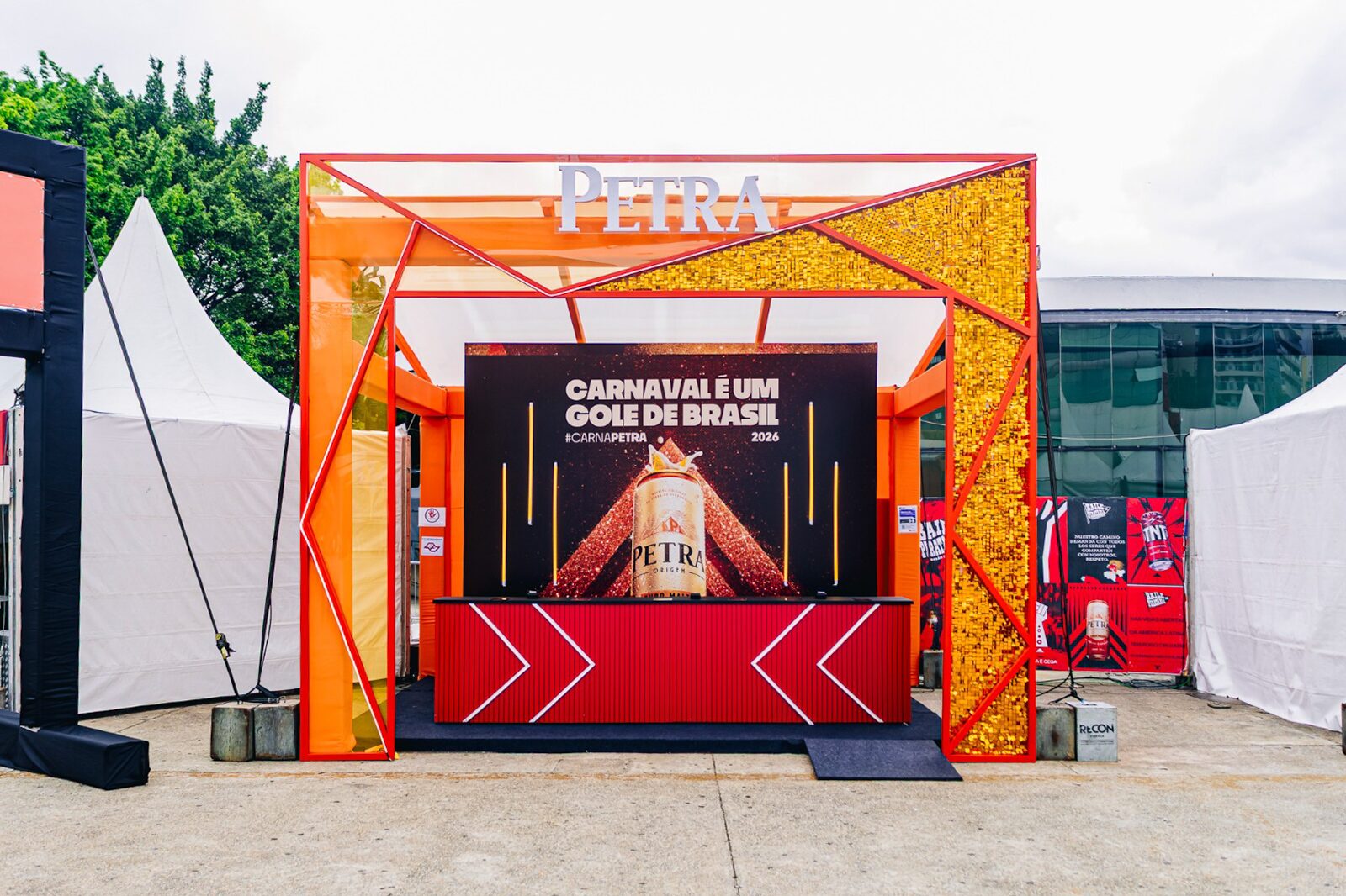 Stand com estrutura geométrica laranja e dourada montado ao ar livre para evento