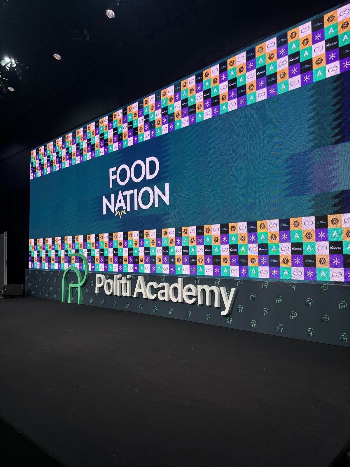 Vista ampla de palco cenográfico com grande painel LED e testeira corporativa em convenção de negócios