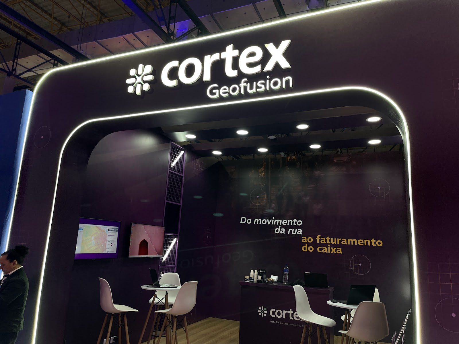 Fachada de stand com arco iluminado e telas de dados em feira de negócios