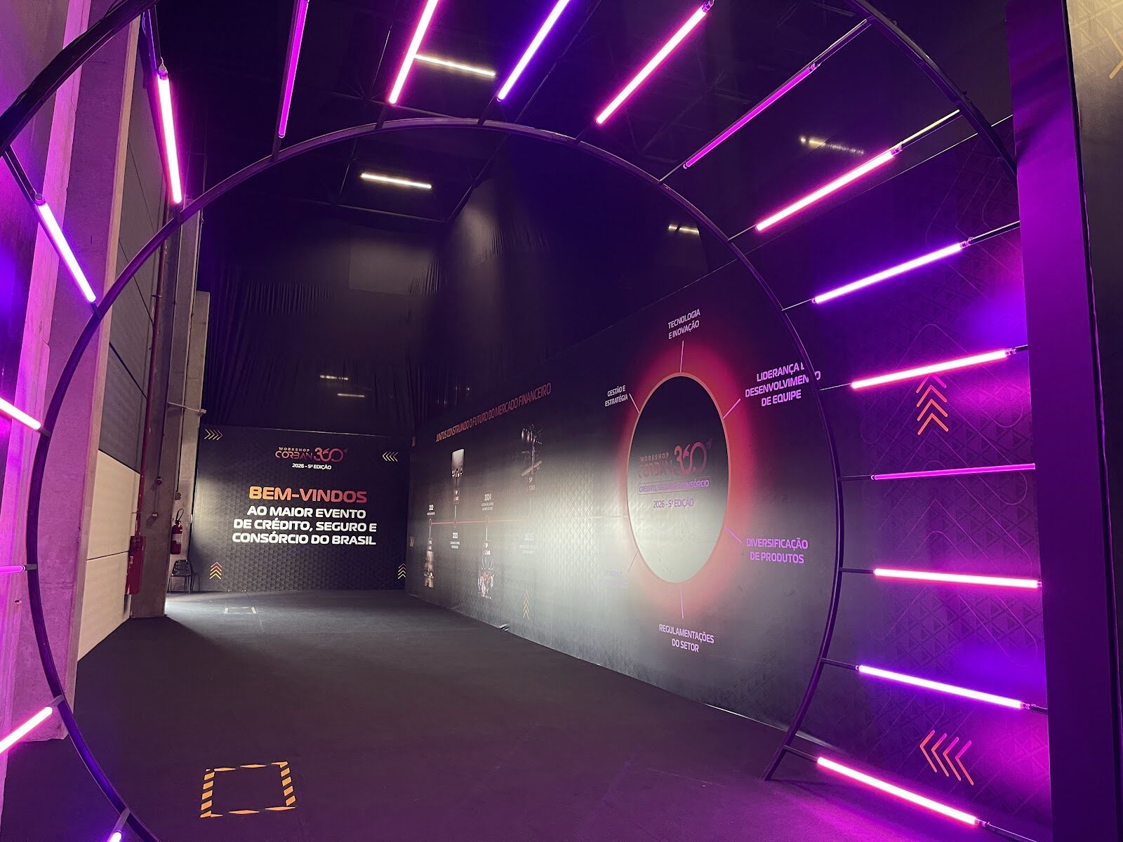Túnel cenográfico com arcos neon rosa e roxo em evento