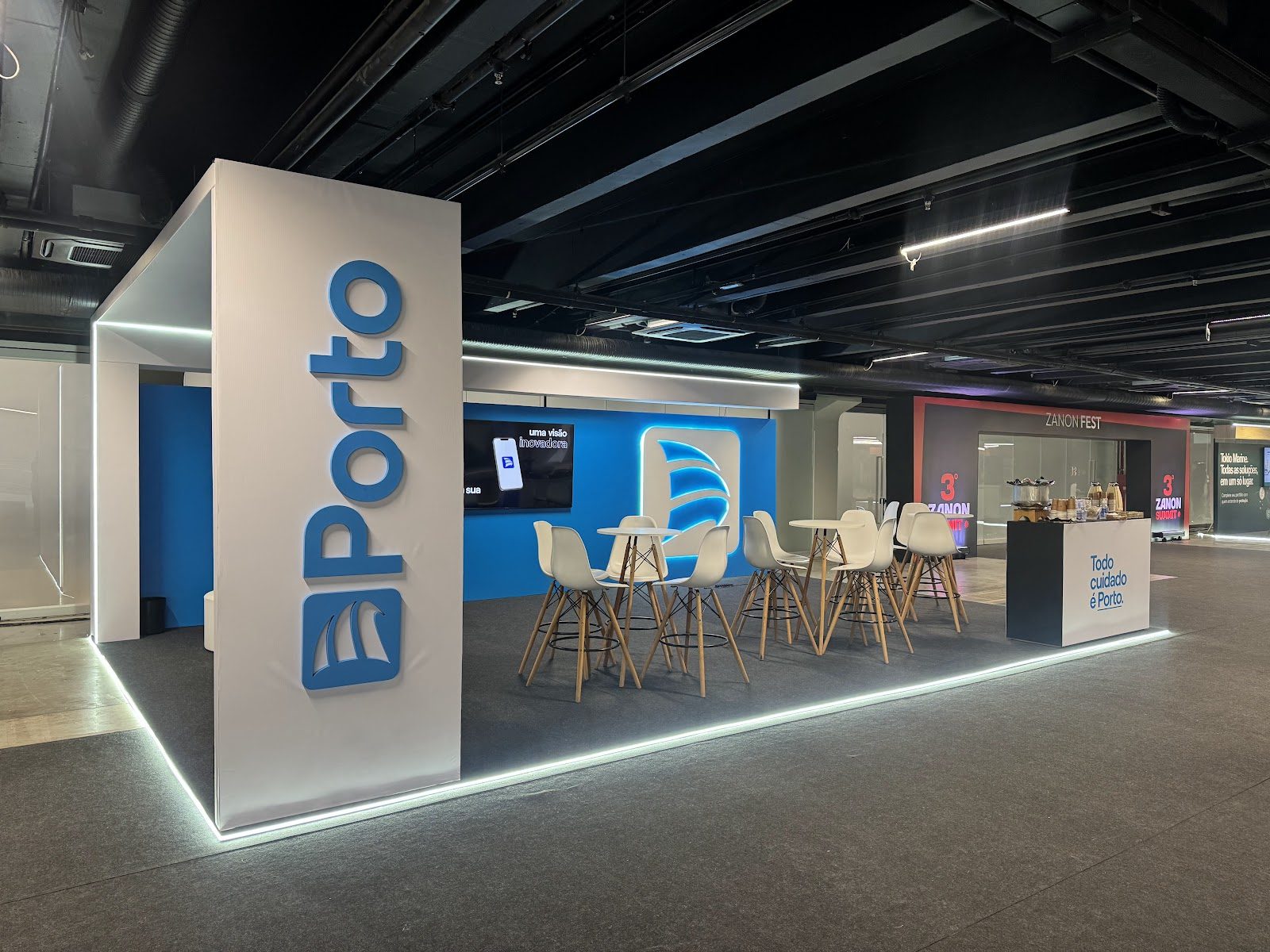 Stand com logotipo em relevo iluminado e área de convivência em feira