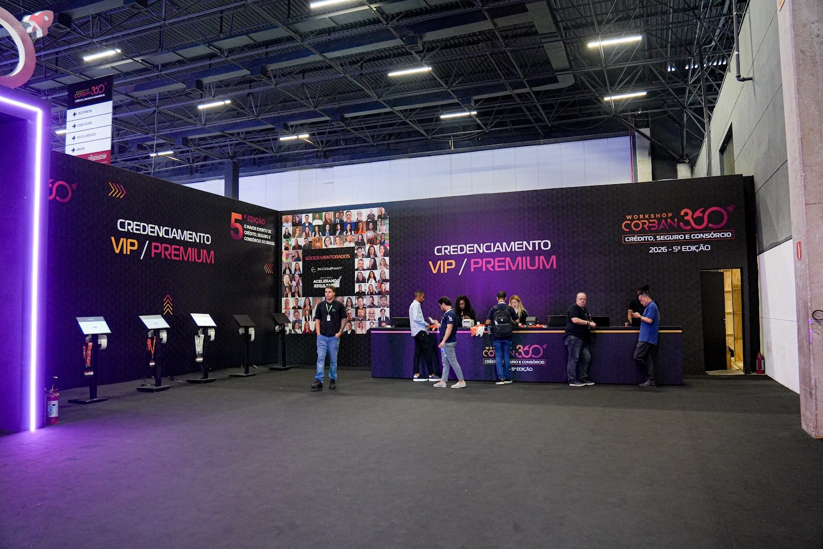 Balcão de credenciamento com painel iluminado e totens em evento corporativo