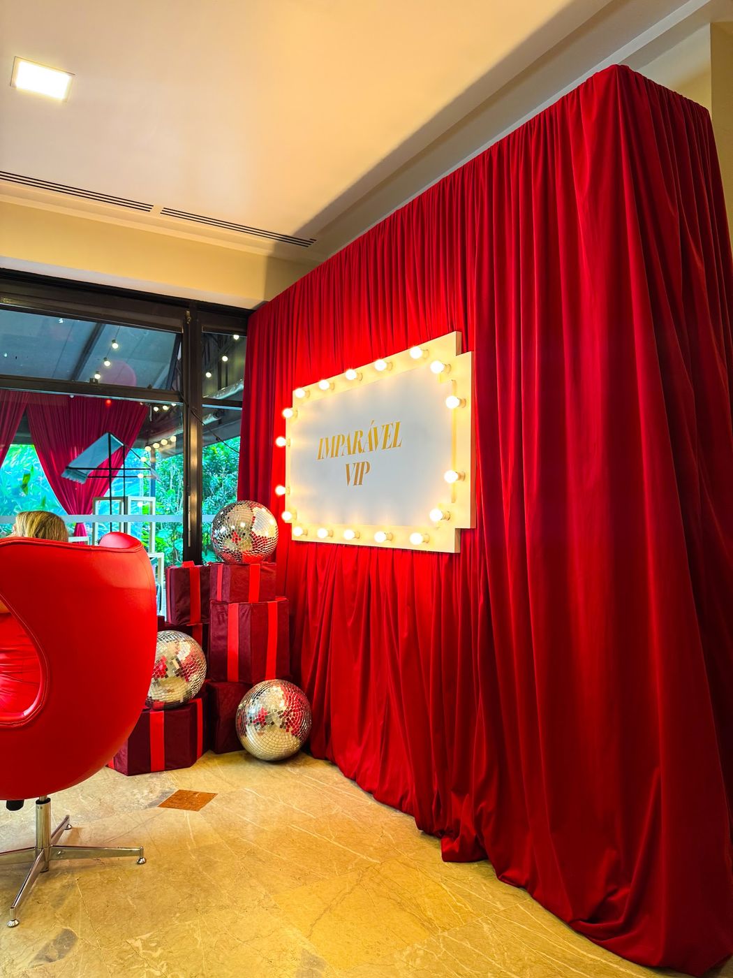 Camarim VIP com cortina vermelha, letreiro luminoso e esferas espelhadas em evento social