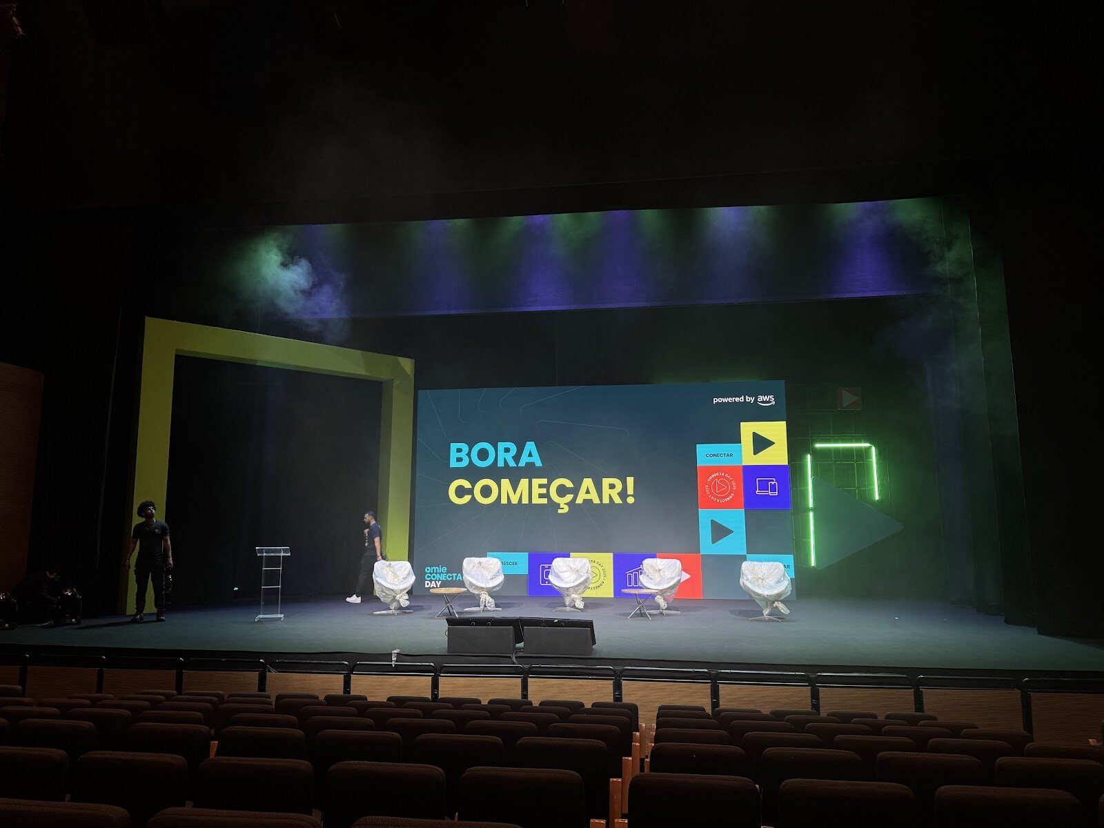 Palco de auditório com portal cenográfico amarelo e moldura neon verde pronto para o início de evento corporativo