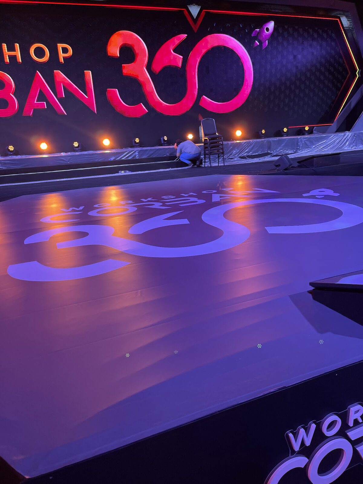 Palco cenográfico em fase de montagem com piso protegido e logotipo projetado antes do evento