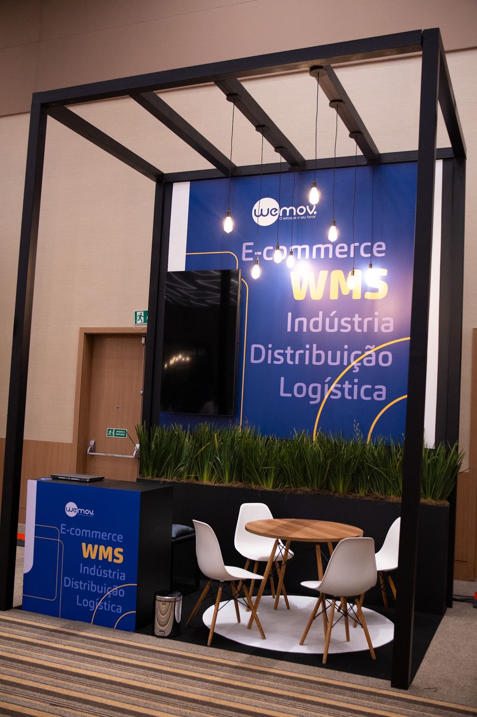 Estande com madeira, luminárias pendentes e jardim vertical em convenção