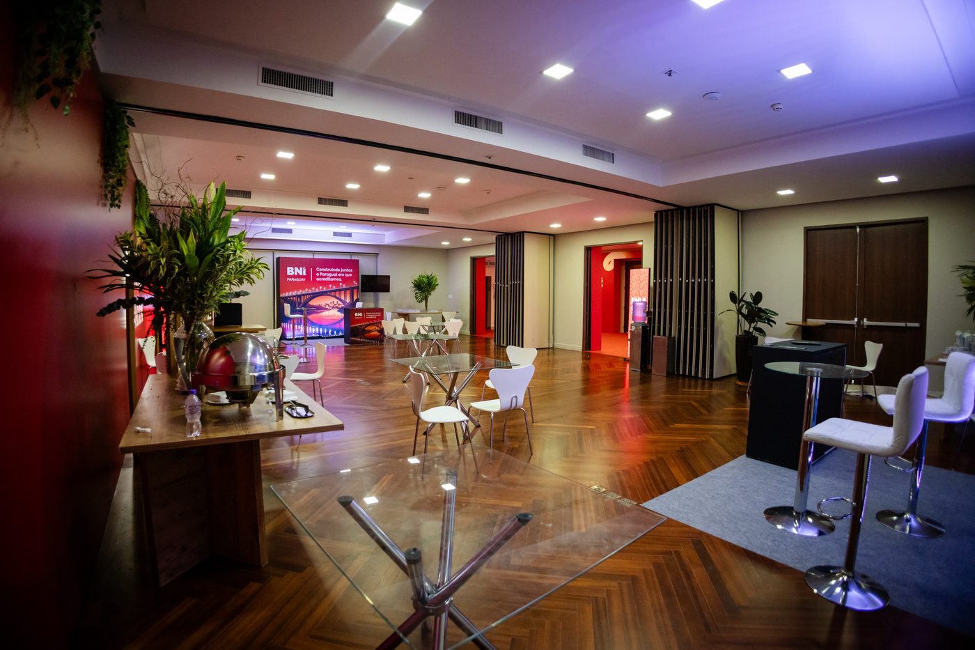 Área de parceiros e lounge de networking do BNI Summit 26 SP, com mesas altas e ambientação em vermelho e branco
