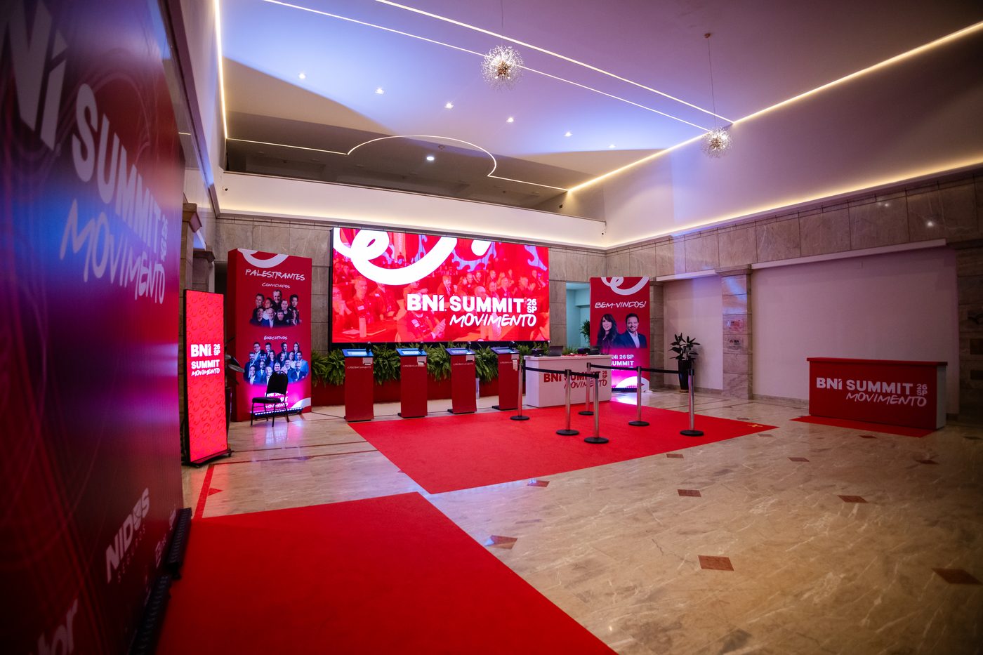 Recepção do BNI Summit 26 SP com mesa de credenciamento, tapete vermelho e telão com o conceito Movimento, projetada pela Atom
