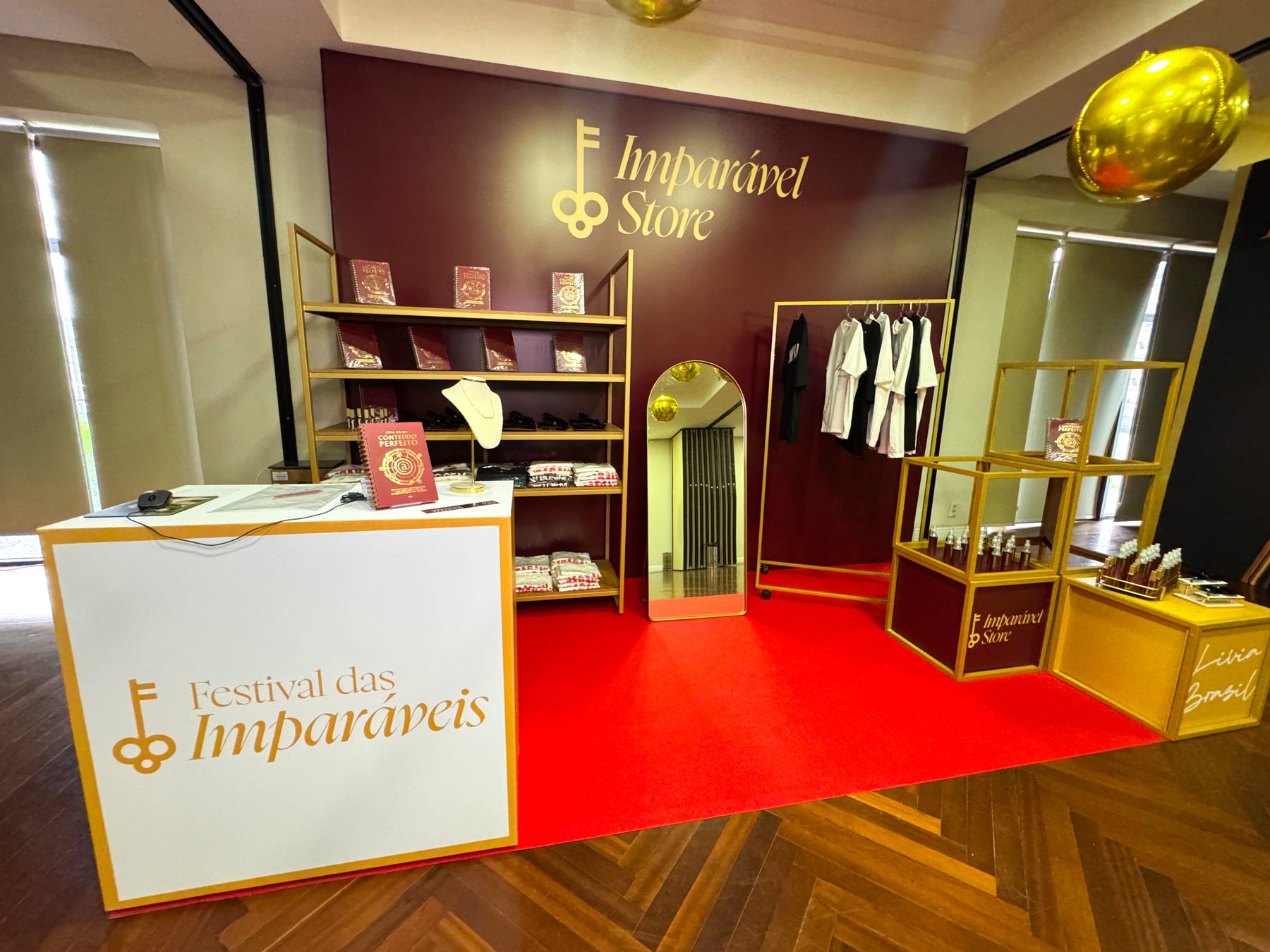 Área de produtos com estante, araras e nichos dourados sobre carpete vermelho, com a marca Imparável Store ao fundo