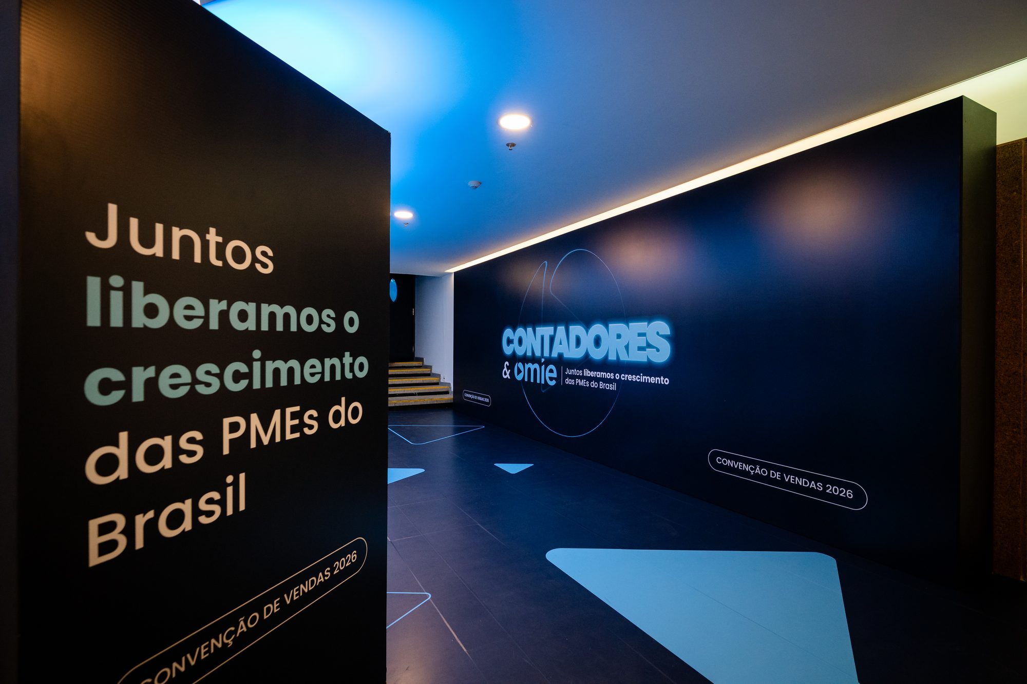 Corredor de entrada da Convenção de Vendas Omie 2026 com backdrop iluminado e sinalização cênica
