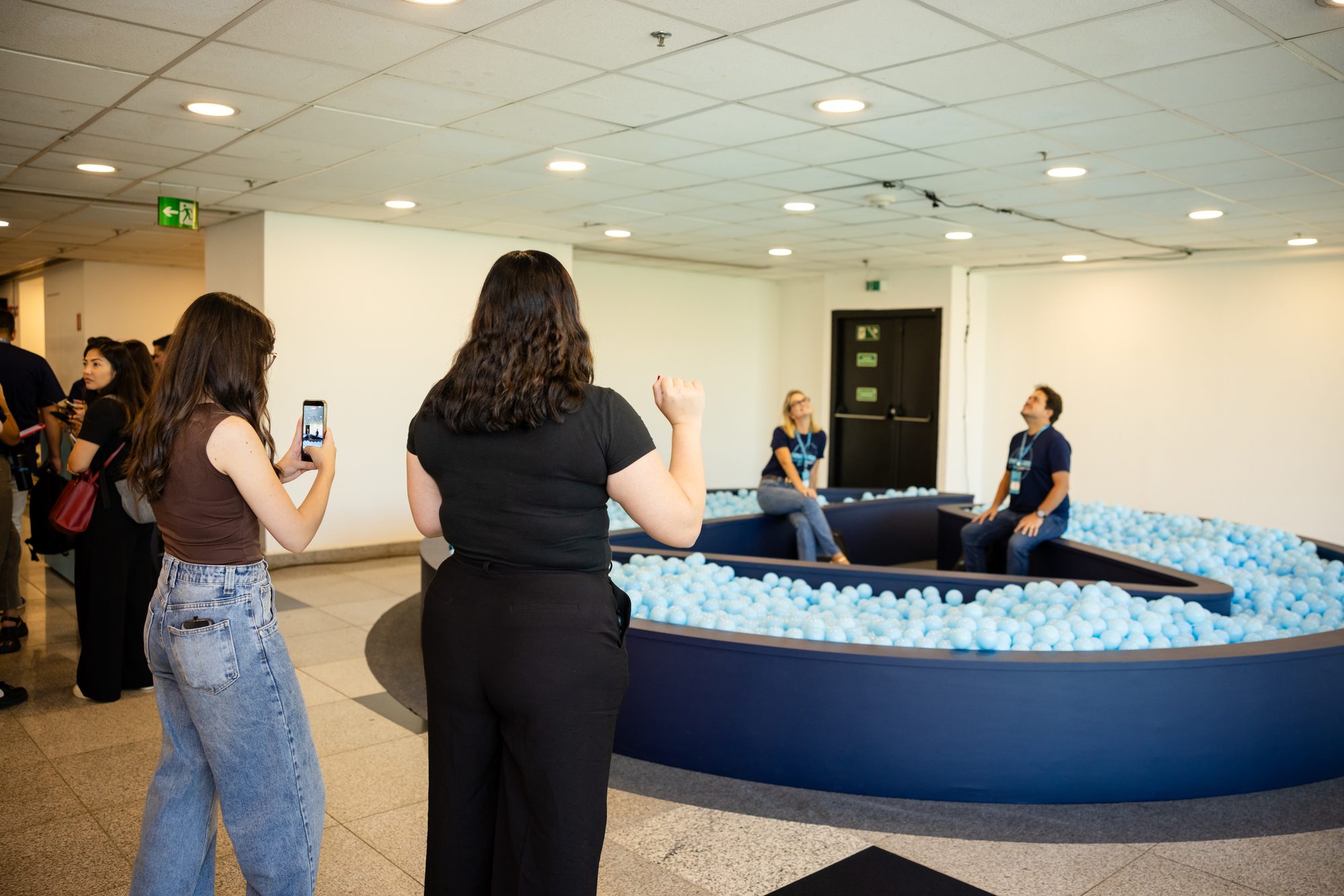 Participantes fotografando e sentados na piscina de bolinhas em formato do símbolo Omie